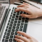 Part-time Job - From above of unrecognizable woman sitting at table and typing on keyboard of computer during remote work in modern workspace