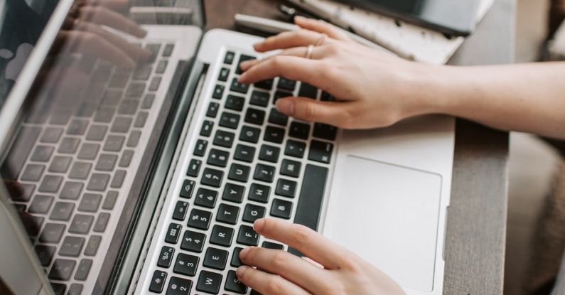 Part-time Job - From above of unrecognizable woman sitting at table and typing on keyboard of computer during remote work in modern workspace