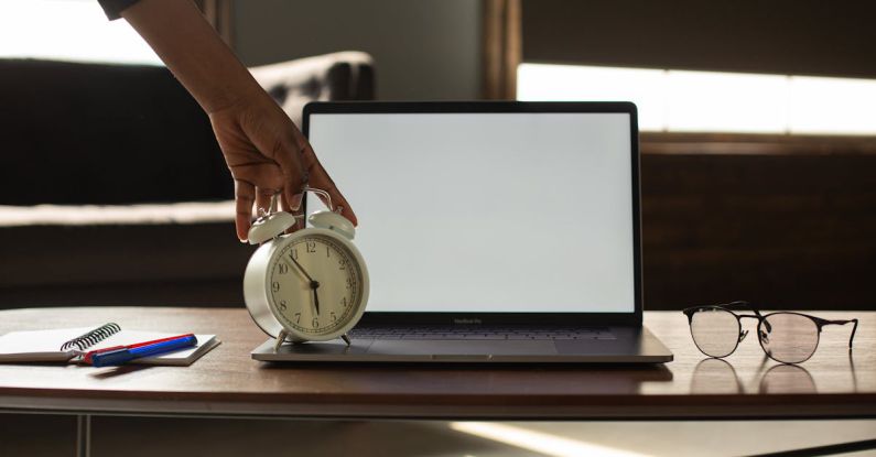 Clock Plan - Anonymous black person touching alarm clock near opened netbook with white blank screen placed on table with notebook and pens