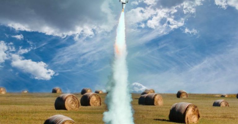 Project Launch - Small model rocket flying up in smoke after launch on green field with hay rolls