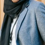 Non-traditional Career - Confident young African American Islamic businesswoman in elegant suit and traditional hijab smiling and looking at camera while standing near corrugated metal wall with hands in pockets