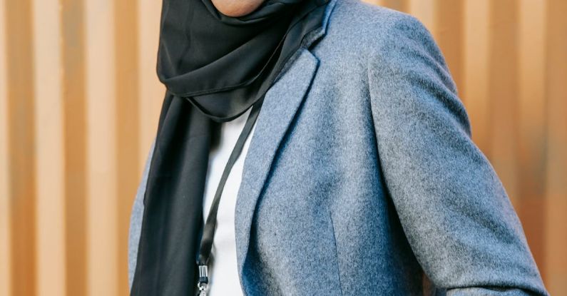 Non-traditional Career - Confident young African American Islamic businesswoman in elegant suit and traditional hijab smiling and looking at camera while standing near corrugated metal wall with hands in pockets