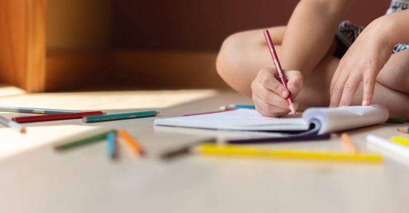 Skills Development - Crop kid sitting on floor and writing in notebook