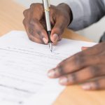 Application Form - Person Holding Gray Twist Pen and White Printer Paper on Brown Wooden Table