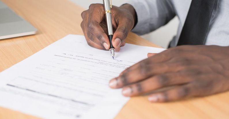 Application Form - Person Holding Gray Twist Pen and White Printer Paper on Brown Wooden Table