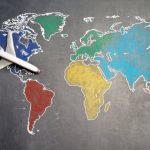 Strategy Plan - Top view of crop anonymous person holding toy airplane on colorful world map drawn on chalkboard